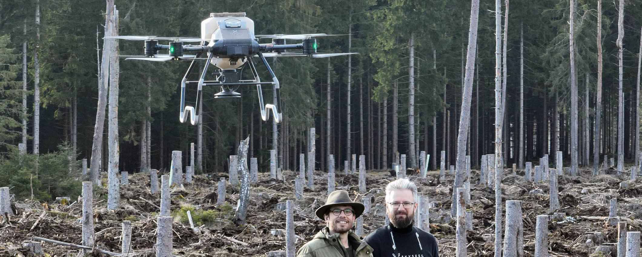 Two people are piloting a Skyseed drone in a forest.